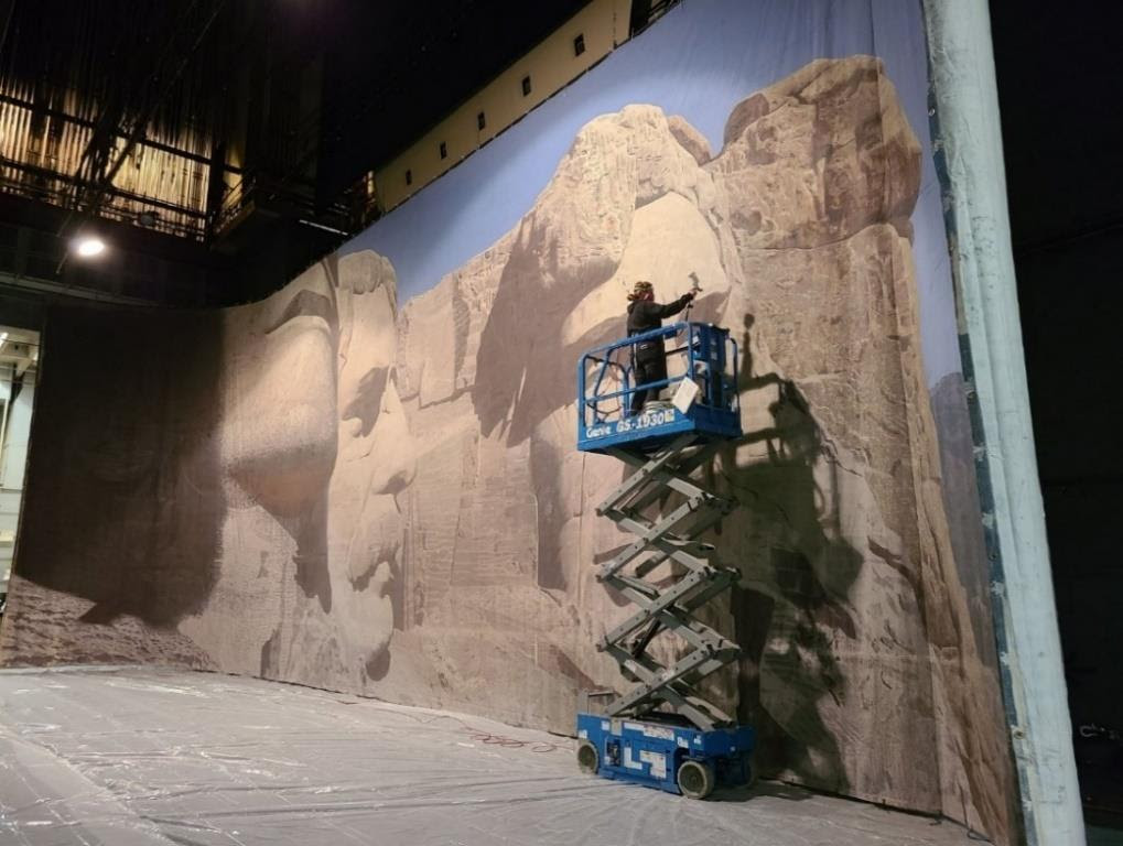 This scenic backdrop is from the 1959 MGM film North By Northwest. Produced and directed by Alfred Hitchcock, the film starred Cary Grant and Eva Marie Saint. Karen L. Maness is pictured above, recently working on the backdrop to prepare it for the upcoming exhibition at the Boca Raton Museum of Art